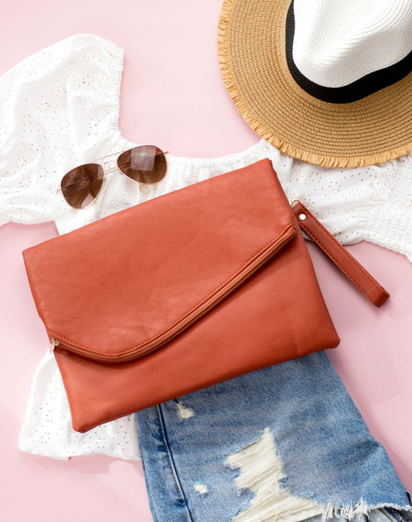 A woman in a white top holds the Foldover Envelope Clutch in black while sitting.