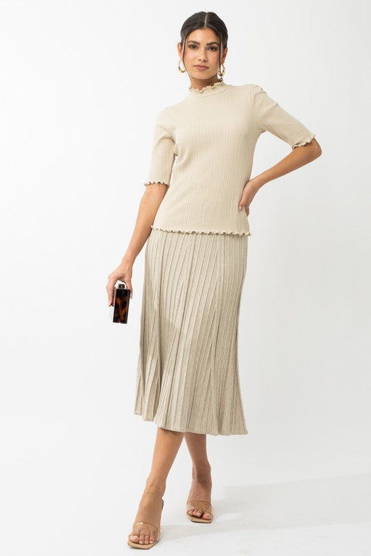 A person in a rust-colored Short Sleeve Mock Neck Merrow Edge Top holds a beige hat. They are also wearing a pleated skirt.