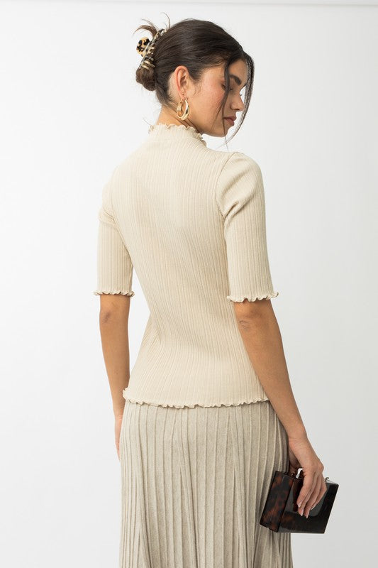 A person in a rust-colored Short Sleeve Mock Neck Merrow Edge Top holds a beige hat. They are also wearing a pleated skirt.