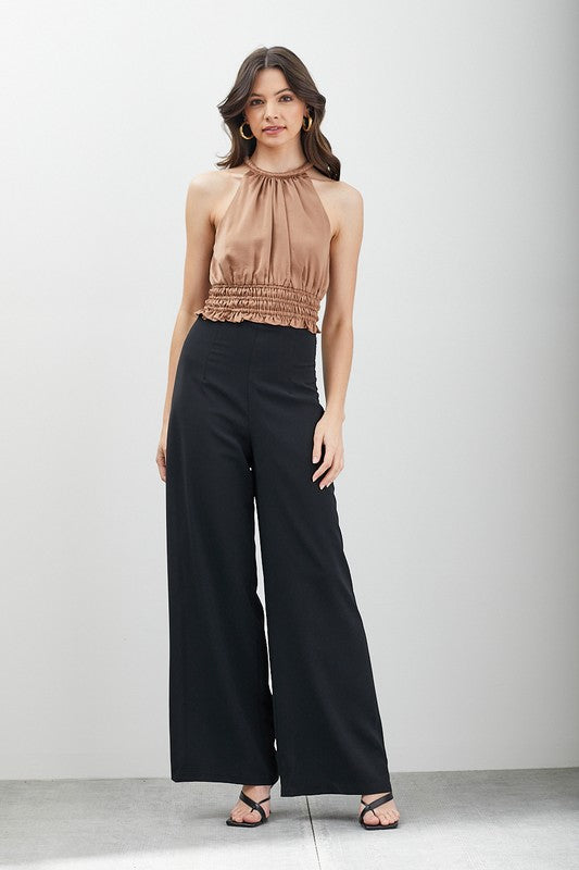 A woman with long hair wearing gold hoop earrings and a beige Smocked Waist Top exudes versatile fashion. Her ensemble is both chic and elegant, making it an ideal choice for any occasion.