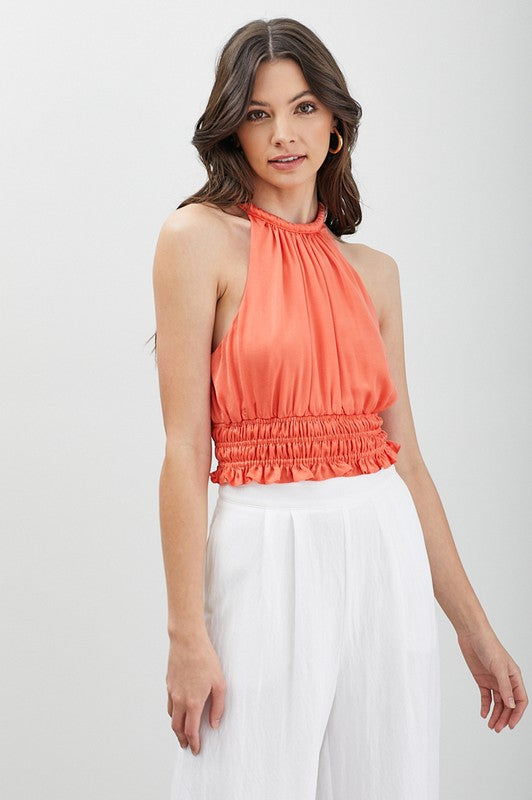 A woman wearing a chic, versatile wardrobe essential—a blue Smocked Waist Top paired with black pants—stands in front of a plain background, highlighting its elegant texture.