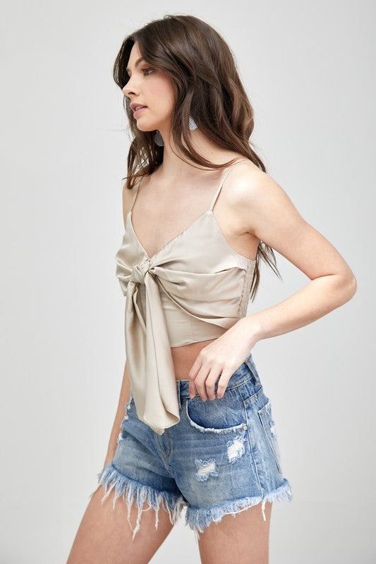 A person wearing a Front Tie-Up Cami Crop Top in light blue, featuring a V-neckline, paired with brown pants stands against a plain background, perfectly capturing the essence of a summer wardrobe.