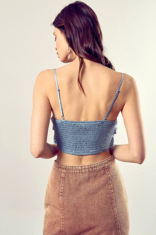 A person wearing a Front Tie-Up Cami Crop Top in light blue, featuring a V-neckline, paired with brown pants stands against a plain background, perfectly capturing the essence of a summer wardrobe.