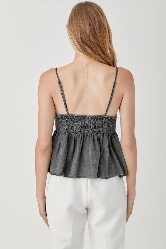 With long, light hair, an individual models a stylish and cozy Smocked Flare Bottom Knit Cami Top paired with white pants against a plain background, capturing the essence of an ideal summer wardrobe.