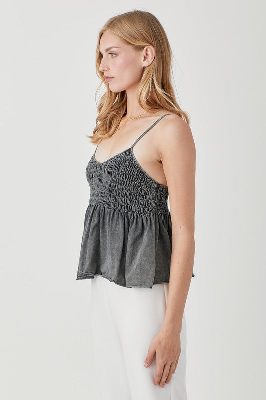 With long, light hair, an individual models a stylish and cozy Smocked Flare Bottom Knit Cami Top paired with white pants against a plain background, capturing the essence of an ideal summer wardrobe.