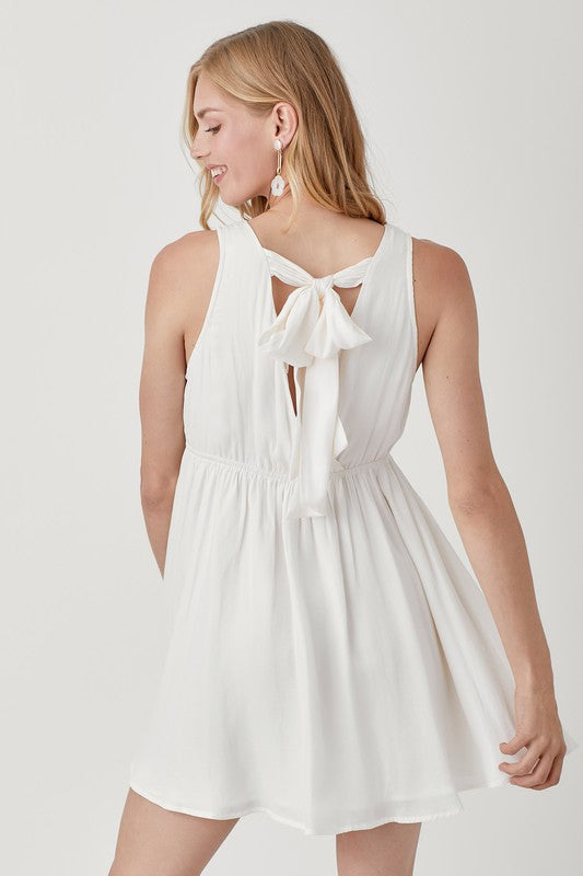 A person wearing the V Neck Smock Sleeveless Dress in white smiles while looking down, their hands gently holding the dress.