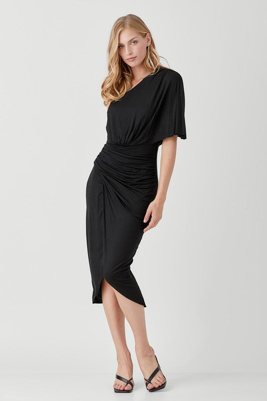 A woman in a chic One Shoulder Drape Jersey Dress poses against a plain background, paired with black sandals.