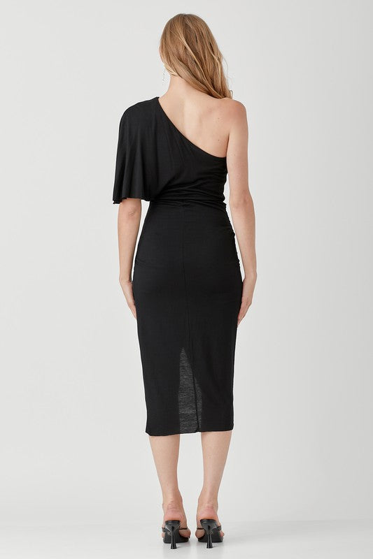 A woman in a chic One Shoulder Drape Jersey Dress poses against a plain background, paired with black sandals.