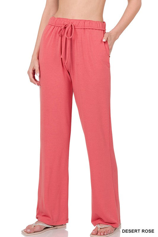 A person stands barefoot on a white background wearing Drawstring Lounge Pants in coral pink, featuring a relaxed fit and drawstring waist.