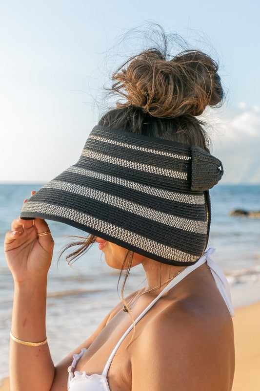 Woman in a white bikini holding her Marled Stripe Roll up Bow Visor while facing the sea.