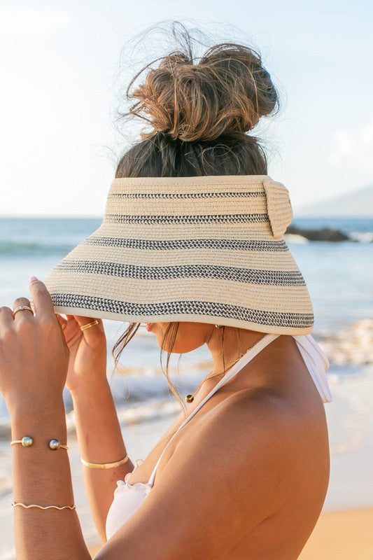 Woman in a white bikini holding her Marled Stripe Roll up Bow Visor while facing the sea.
