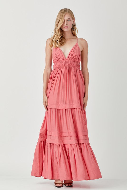 Dressed in a Shirred Ruffle Folded Detail Maxi Dress, featuring a striking blue color, plunging neckline, and stylish ruffle accents, the individual stands against a plain background exuding an effortless boho style.