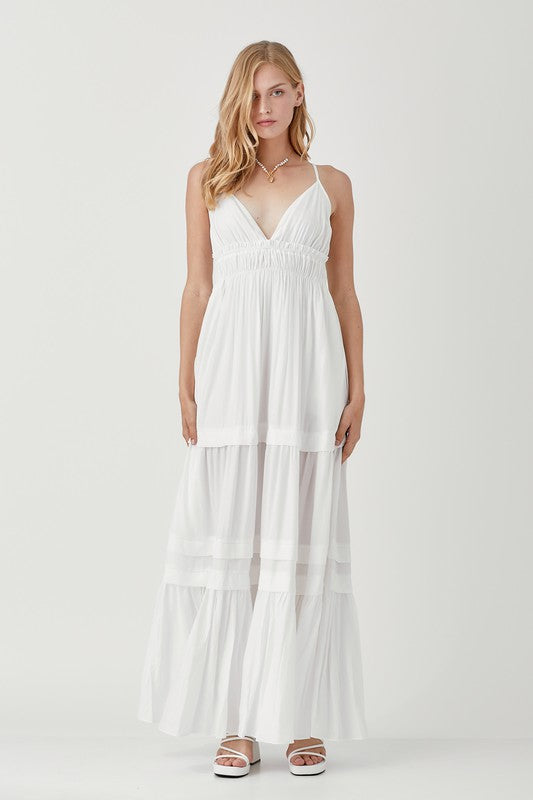 Dressed in a Shirred Ruffle Folded Detail Maxi Dress, featuring a striking blue color, plunging neckline, and stylish ruffle accents, the individual stands against a plain background exuding an effortless boho style.