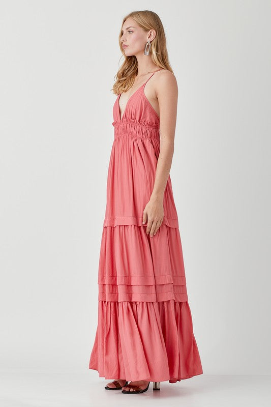 Dressed in a Shirred Ruffle Folded Detail Maxi Dress, featuring a striking blue color, plunging neckline, and stylish ruffle accents, the individual stands against a plain background exuding an effortless boho style.