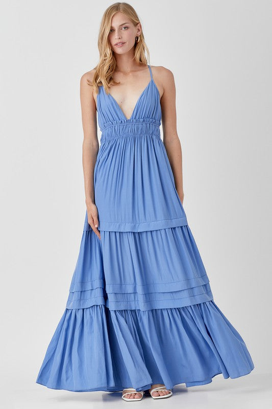 Dressed in a Shirred Ruffle Folded Detail Maxi Dress, featuring a striking blue color, plunging neckline, and stylish ruffle accents, the individual stands against a plain background exuding an effortless boho style.