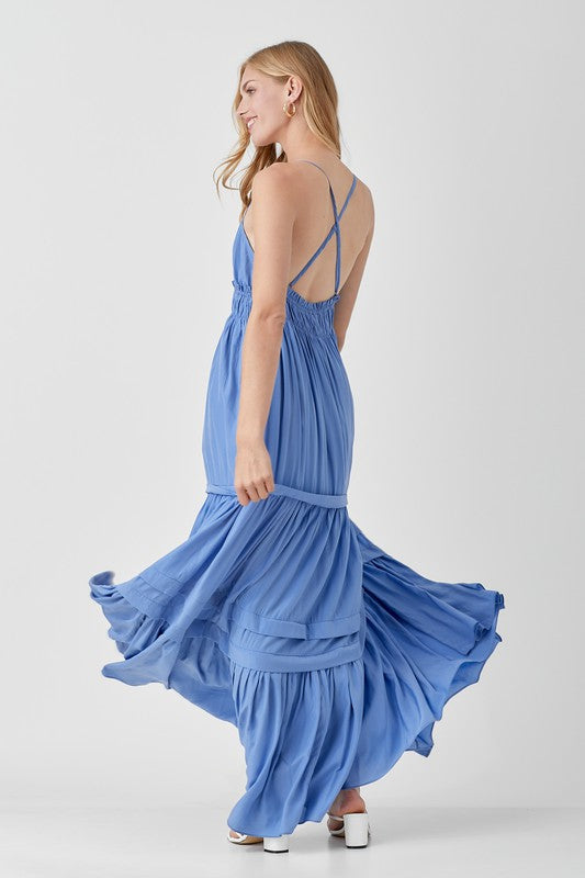 Dressed in a Shirred Ruffle Folded Detail Maxi Dress, featuring a striking blue color, plunging neckline, and stylish ruffle accents, the individual stands against a plain background exuding an effortless boho style.