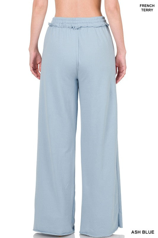 Against a plain white backdrop, someone models the French Terry Drawstring Waist Raw Edge Hem Pants in light blue. The wide-leg design and soft fabric provide a relaxed style, while the drawstring waist enhances comfort for any casual gathering.