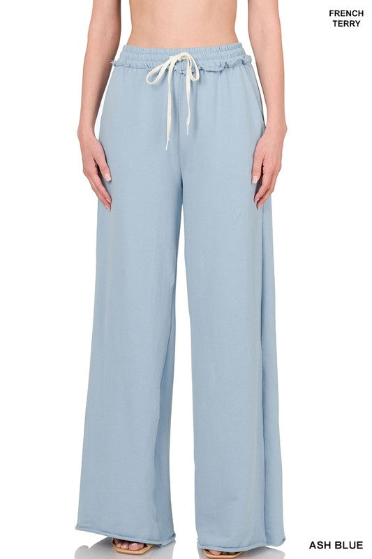 Against a plain white backdrop, someone models the French Terry Drawstring Waist Raw Edge Hem Pants in light blue. The wide-leg design and soft fabric provide a relaxed style, while the drawstring waist enhances comfort for any casual gathering.