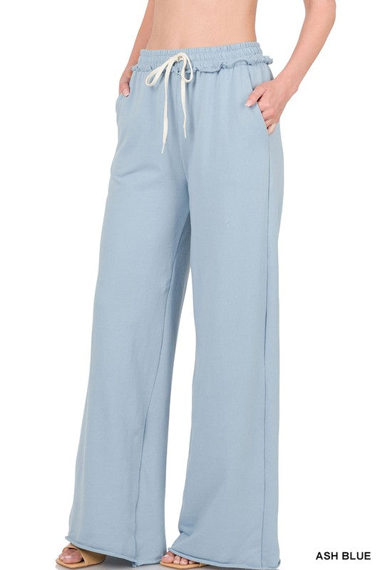 Against a plain white backdrop, someone models the French Terry Drawstring Waist Raw Edge Hem Pants in light blue. The wide-leg design and soft fabric provide a relaxed style, while the drawstring waist enhances comfort for any casual gathering.