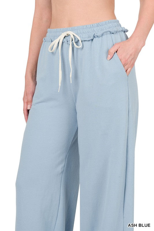 Against a plain white backdrop, someone models the French Terry Drawstring Waist Raw Edge Hem Pants in light blue. The wide-leg design and soft fabric provide a relaxed style, while the drawstring waist enhances comfort for any casual gathering.