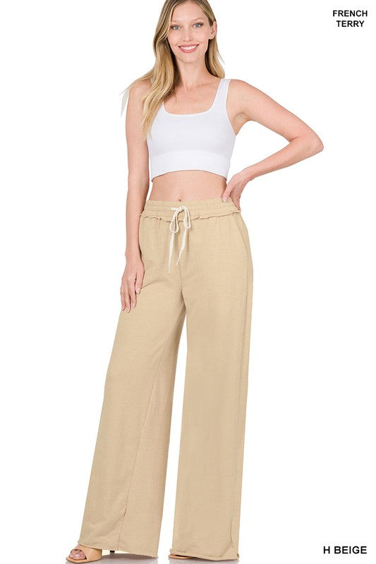 Against a plain white backdrop, someone models the French Terry Drawstring Waist Raw Edge Hem Pants in light blue. The wide-leg design and soft fabric provide a relaxed style, while the drawstring waist enhances comfort for any casual gathering.