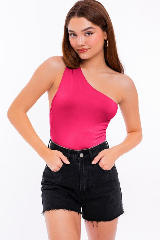 A person exudes chic style in a beige One Shoulder Bodysuit paired with fitted black denim shorts, posing elegantly against a white background.