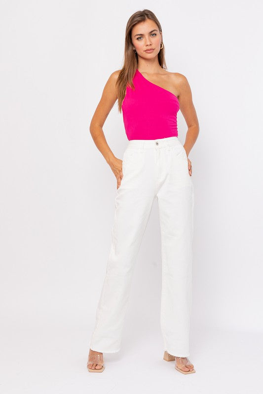 A person exudes chic style in a beige One Shoulder Bodysuit paired with fitted black denim shorts, posing elegantly against a white background.