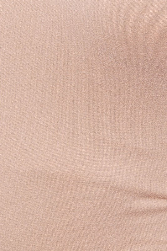 A person exudes chic style in a beige One Shoulder Bodysuit paired with fitted black denim shorts, posing elegantly against a white background.