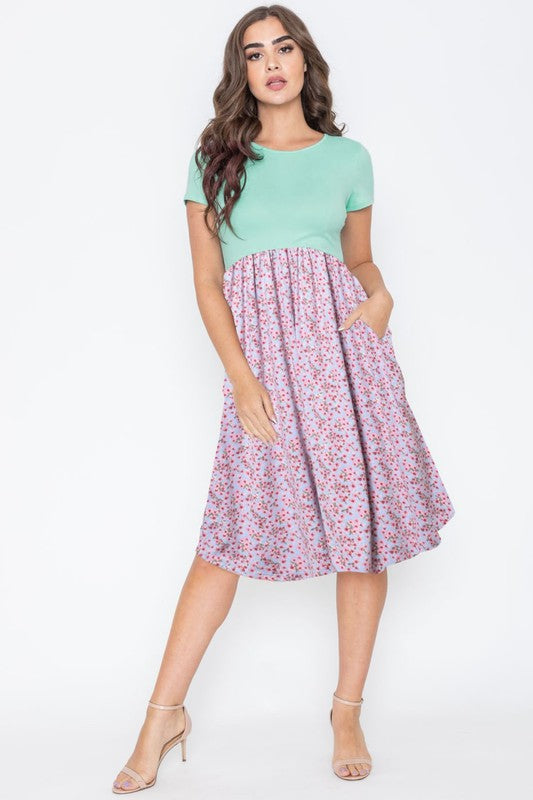 A woman elegantly poses against a simple backdrop, wearing the Plus Short Sleeve Floral Midi Dress. Her long hair cascades down as she stands tall in strappy heels, embodying effortless grace.