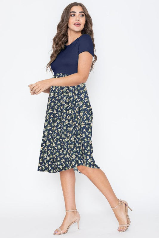 A person wearing the Short Sleeve Floral Midi Dress in navy, featuring short sleeves and crafted with pride in the United States, stands against a plain background.