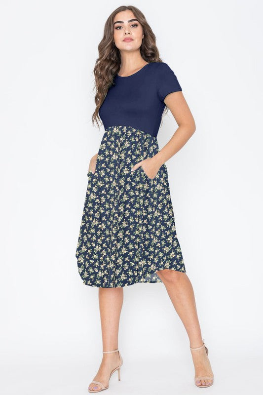 A person wearing the Short Sleeve Floral Midi Dress in navy, featuring short sleeves and crafted with pride in the United States, stands against a plain background.