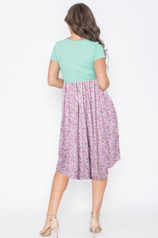 A woman elegantly poses against a simple backdrop, wearing the Plus Short Sleeve Floral Midi Dress. Her long hair cascades down as she stands tall in strappy heels, embodying effortless grace.