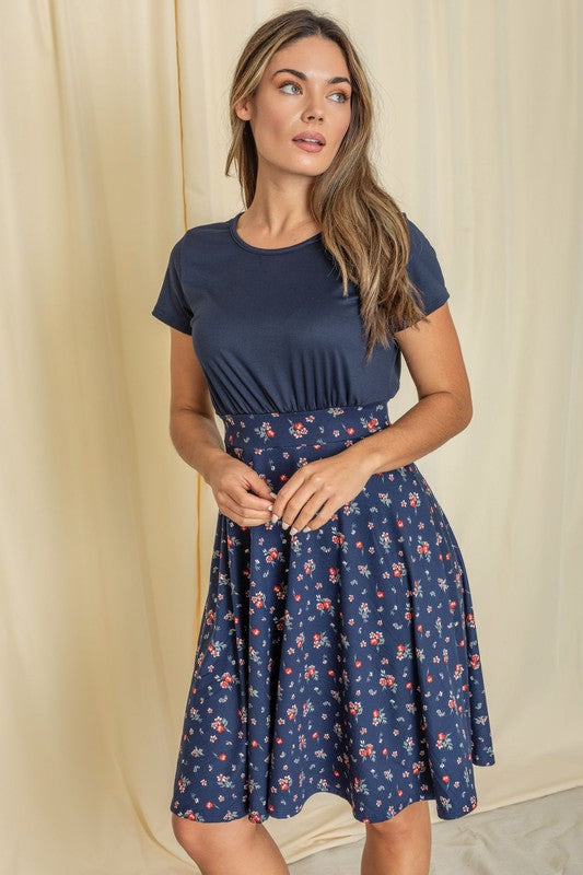 A woman in a vibrant purple top and a Plus Floral Band Flare Dress smiles against a light-colored background, proudly showcasing an outfit made in the United States.