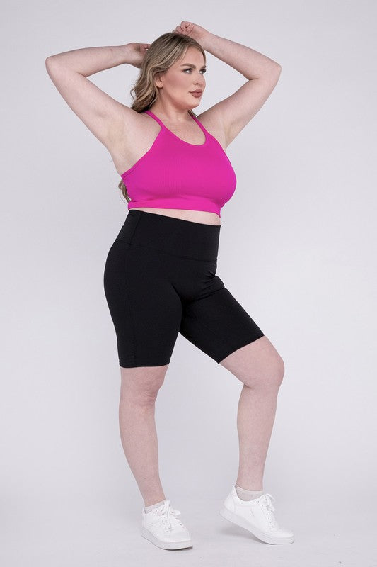 Against a plain background, a person showcases the Plus Athletic High Rise Biker Shorts in coral, crafted from high-quality athletic fabric and paired with a pink top.