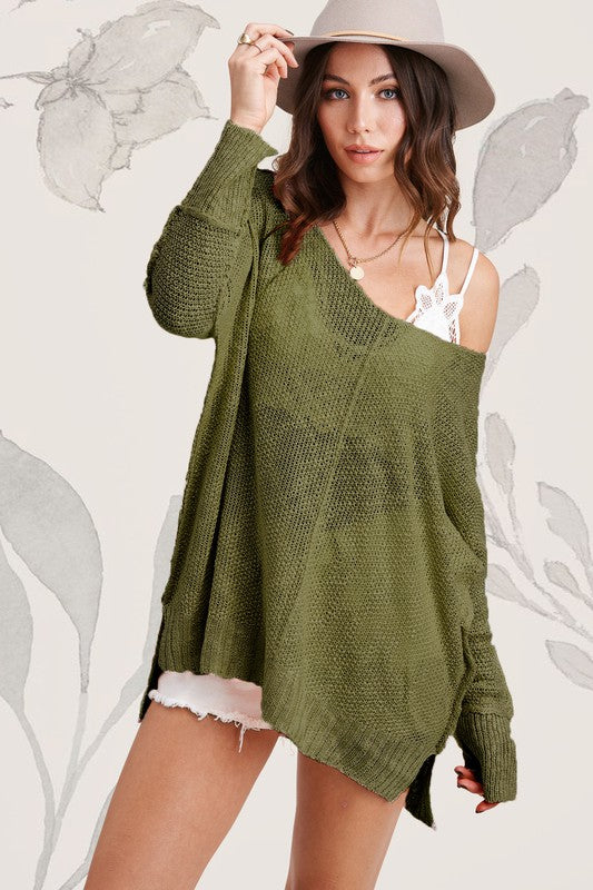 A woman wearing the oversized, stretchy Taylor Sweater in green, paired with a white v-neck lace camisole, white shorts, and a gray hat poses against a neutral background with floral illustrations.