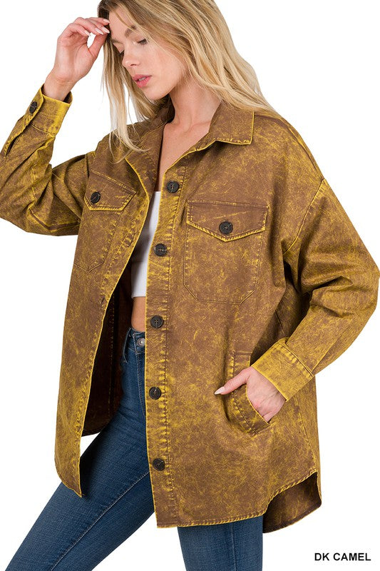 A woman wears a brown Premium Cotton Woven Vintage Washed Shacket with large buttons and front pockets over a white top, paired with blue jeans. Holding her hand near her head, she effortlessly nails casual layered outfits. The label reads “DK CAMEL,” hinting at the timeless charm of this vintage washed shacket.