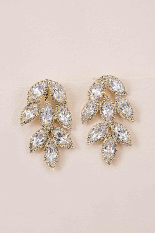 Lana Drop Earrings, showcasing leaf-shaped crystal designs set in a gold petaled frame, displayed on a beige surface.