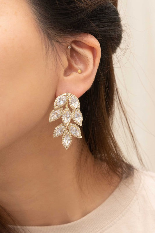 Lana Drop Earrings, showcasing leaf-shaped crystal designs set in a gold petaled frame, displayed on a beige surface.