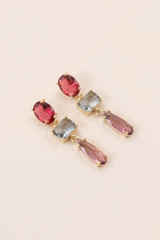 The Fraise Dangle Earrings feature red and blue rectangular, as well as purple teardrop gemstones, elegantly arranged on a white surface. With 10k gold plating, these stunning earrings are perfect for adding a touch of formal style to any outfit.