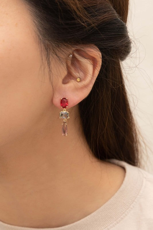 The Fraise Dangle Earrings feature red and blue rectangular, as well as purple teardrop gemstones, elegantly arranged on a white surface. With 10k gold plating, these stunning earrings are perfect for adding a touch of formal style to any outfit.