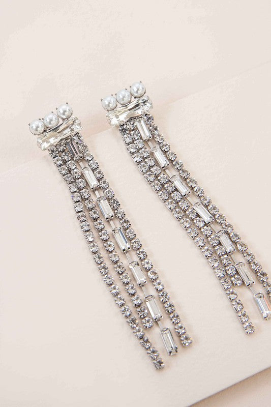 Close-up of a person wearing Gatsby Dangle Earrings, featuring long sterling silver strands adorned with small gems, set against a neutral background.