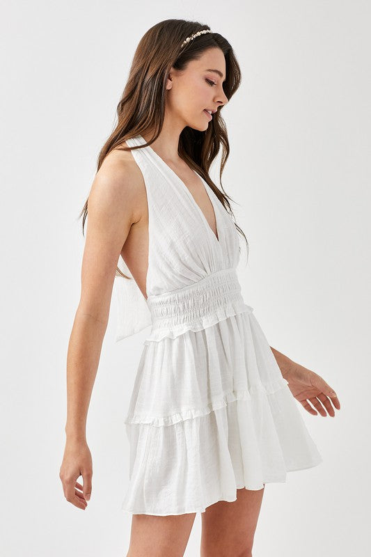 A woman showcases the stylish Halter Neck Smocked Ruffle Dress in blue, gracefully posing with one hand on her hip against a plain backdrop.