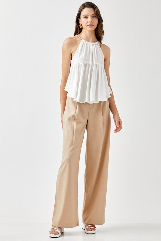 A woman wearing a Halter Neck with Back Strap Flared Top and beige pants stands against a plain background, with one hand on her hip.