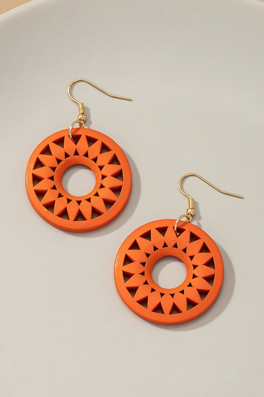 The NEW COLORS Cutout wood circle drop earrings, showcasing exquisite geometric patterns in black, brown, yellow, and orange, are elegantly arranged on a white surface.