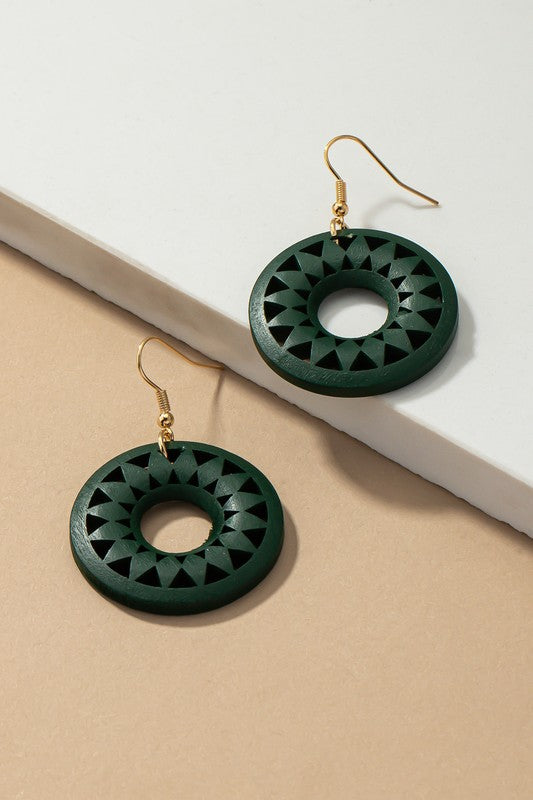 The NEW COLORS Cutout wood circle drop earrings, showcasing exquisite geometric patterns in black, brown, yellow, and orange, are elegantly arranged on a white surface.