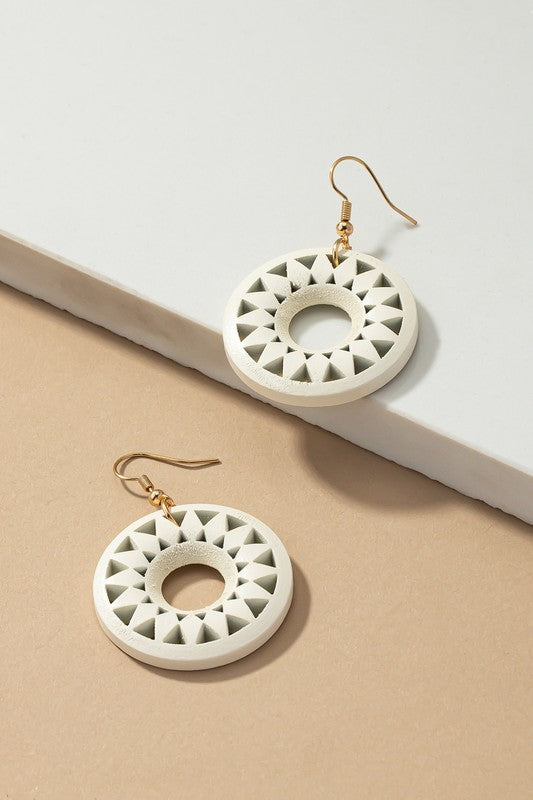 The NEW COLORS Cutout wood circle drop earrings, showcasing exquisite geometric patterns in black, brown, yellow, and orange, are elegantly arranged on a white surface.