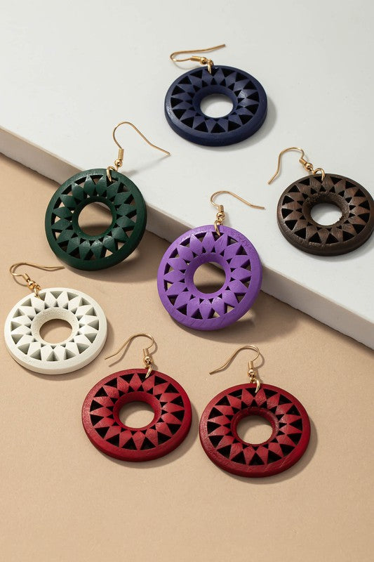 The NEW COLORS Cutout wood circle drop earrings, showcasing exquisite geometric patterns in black, brown, yellow, and orange, are elegantly arranged on a white surface.