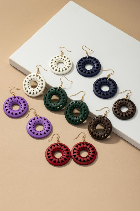 The NEW COLORS Cutout wood circle drop earrings, showcasing exquisite geometric patterns in black, brown, yellow, and orange, are elegantly arranged on a white surface.