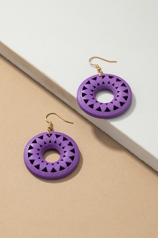 The NEW COLORS Cutout wood circle drop earrings, showcasing exquisite geometric patterns in black, brown, yellow, and orange, are elegantly arranged on a white surface.