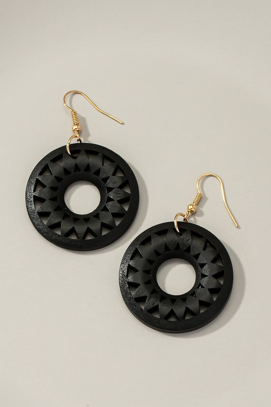 The NEW COLORS Cutout wood circle drop earrings, showcasing exquisite geometric patterns in black, brown, yellow, and orange, are elegantly arranged on a white surface.